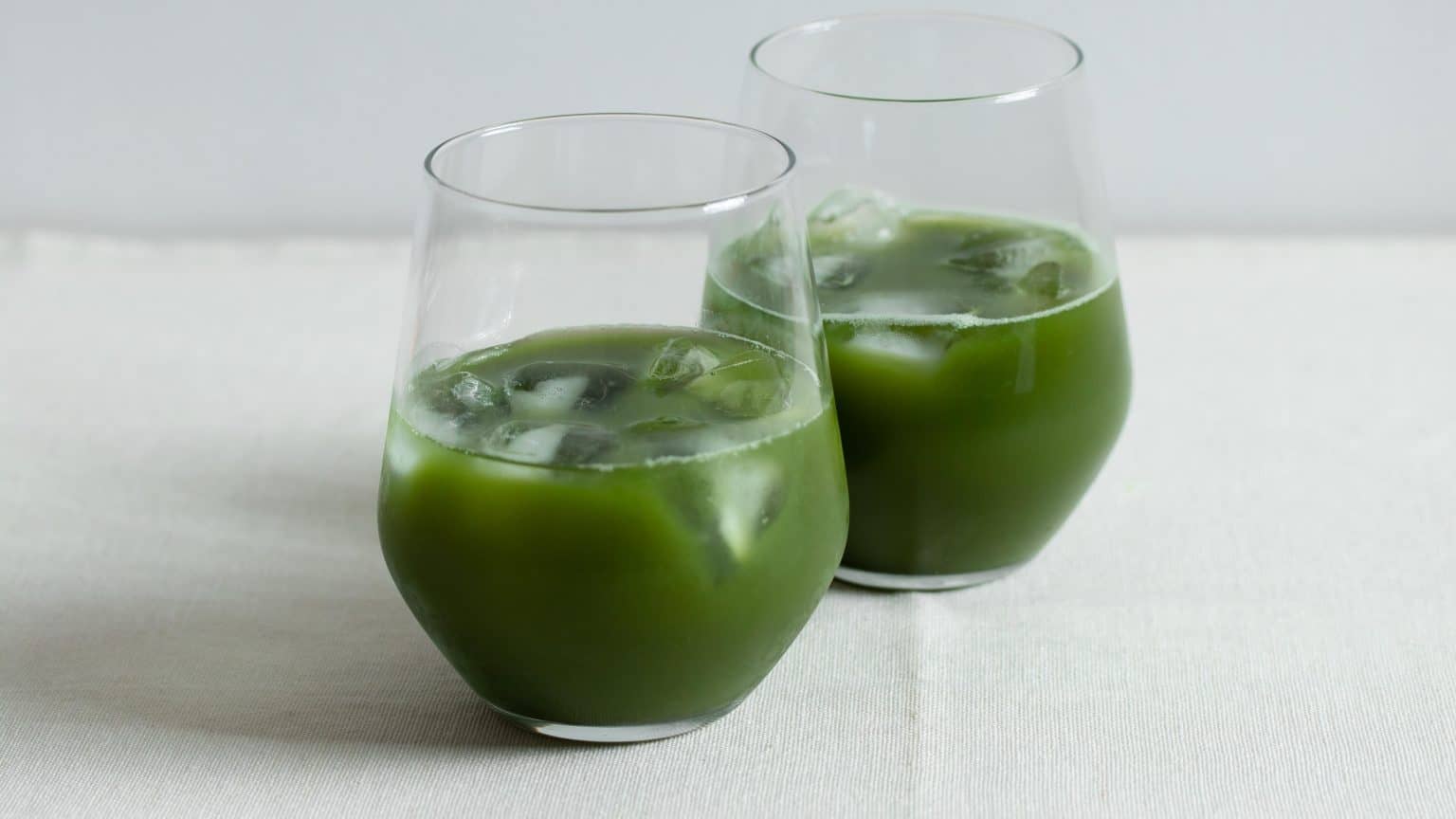 Two stemless glasses with ice and bright green cold brew matcha on a light table.