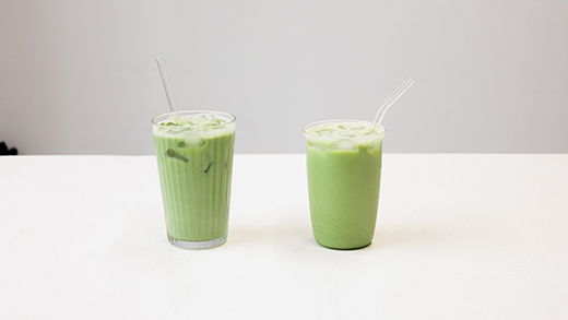 Two green matcha drinks with straws in clear glasses on a white table.