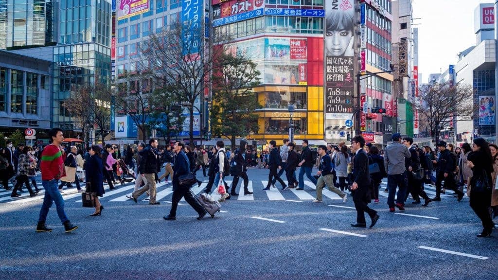 Crowded Shibuya crosswalk in Tokyo with pedestrians crossing amid tall buildings and colorful signs.