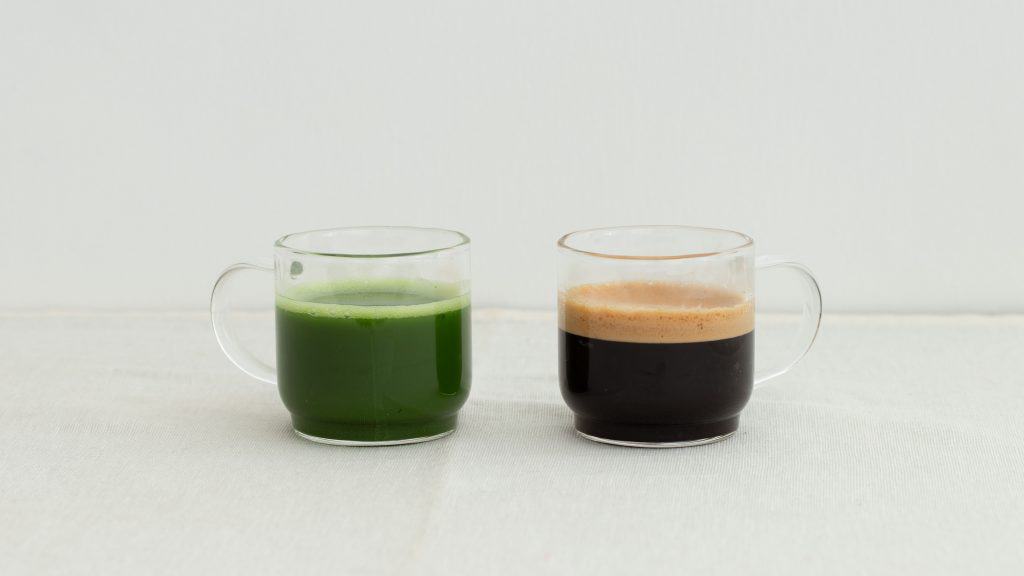 Green matcha tea and dark coffee in two glass mugs side by side on a light surface.
