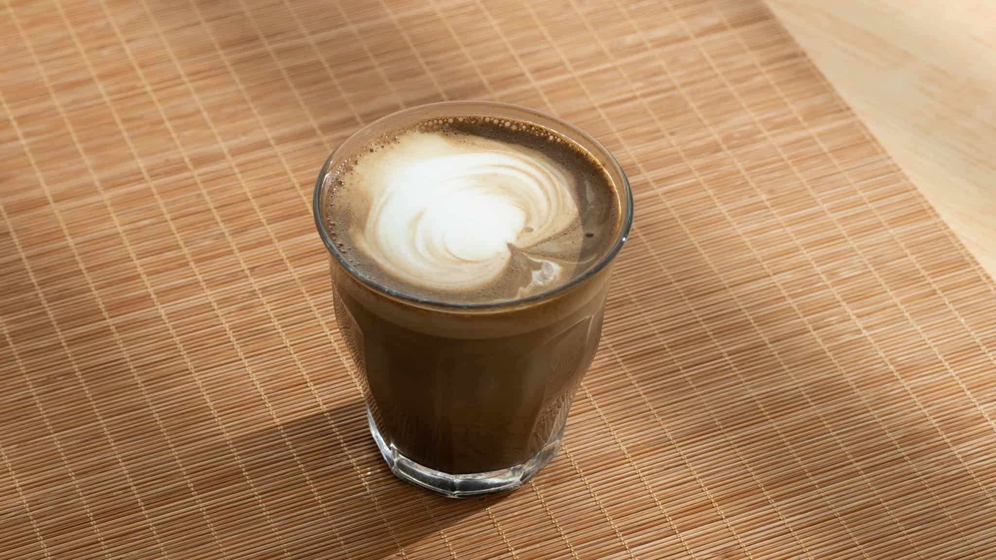 Glass of hojicha latte with a creamy milk swirl on top on a bamboo placemat