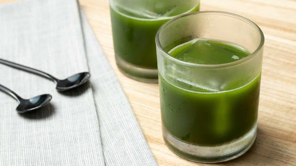 Iced matcha coconut water in a glass on a wooden table with a second glass in the background.