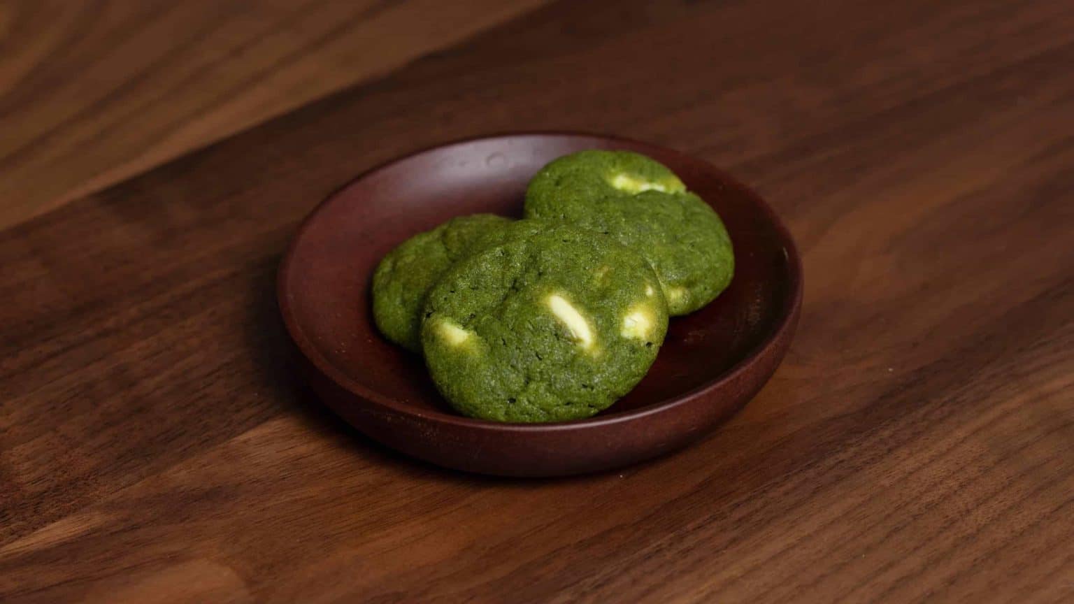 Matcha green tea cookies with white chocolate chips on a dark wooden plate