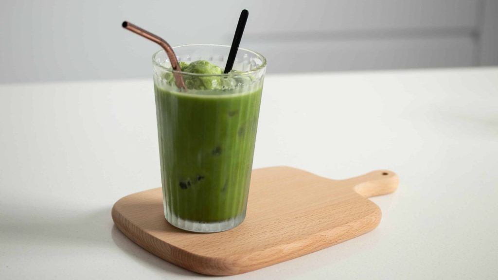 Green matcha ice cream float in a tall glass with two straws on a wooden board.