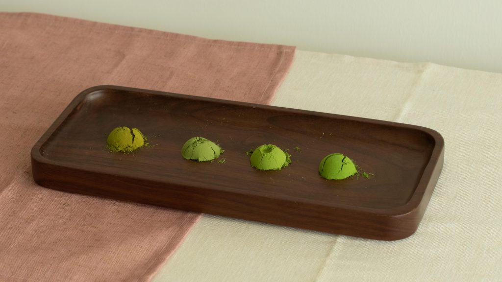 Four green matcha truffles arranged on a dark wooden tray