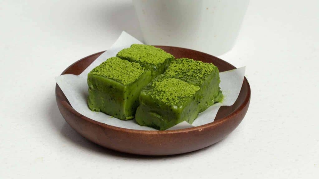 Green matcha Nama chocolate cubes dusted with matcha powder on a small brown plate.
