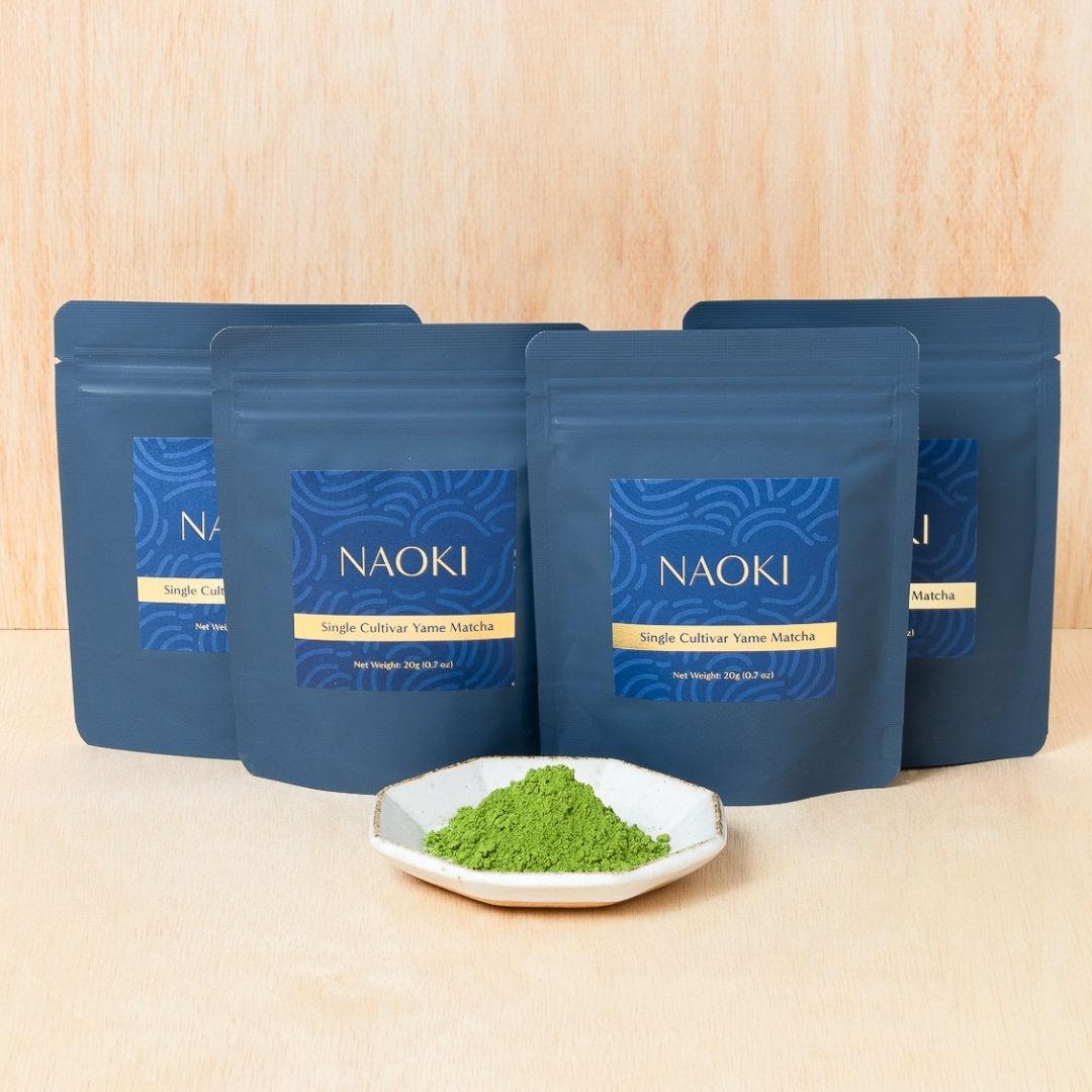 Four blue Naoki Yame single cultivar matcha pouches with a small dish of bright green matcha powder.